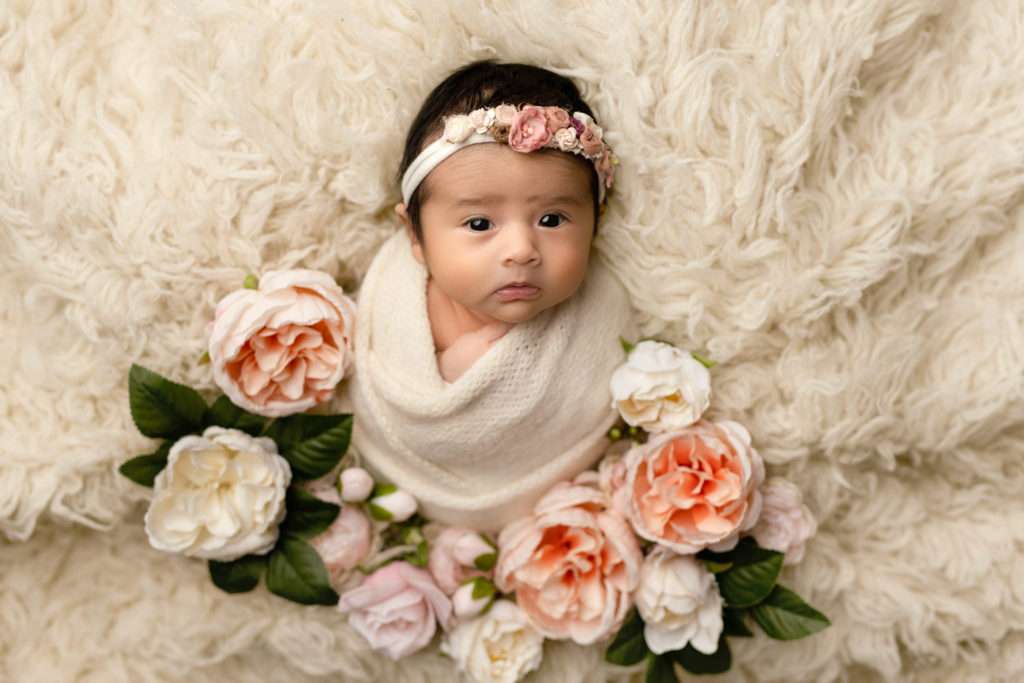 Newborn baby girl on fluffy blanket and flowers
