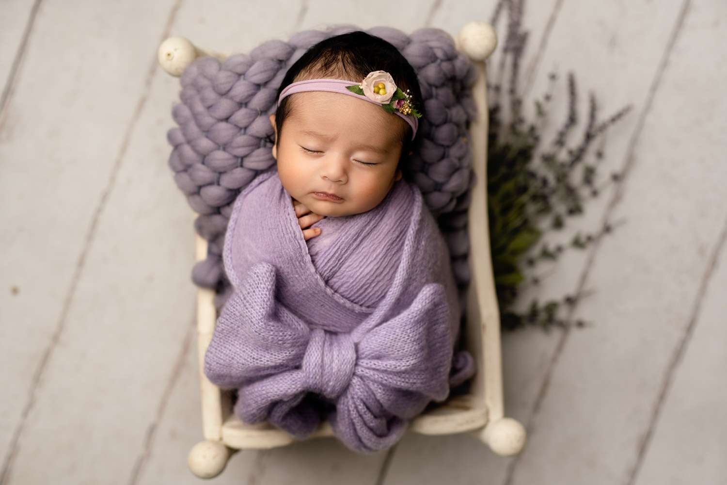 newborn baby girl in purple sleeping in a newborn bed