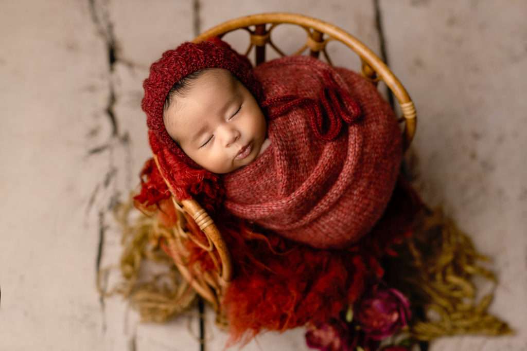 newborn baby girl in a burgundy wrap sleeping in the chair