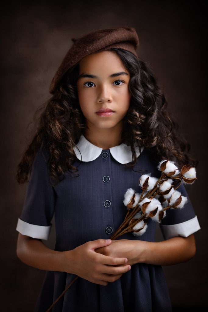 fine art portrait of a girl holding cotton flowers and wearing a blue dress and brown beret in san diego photo studio
