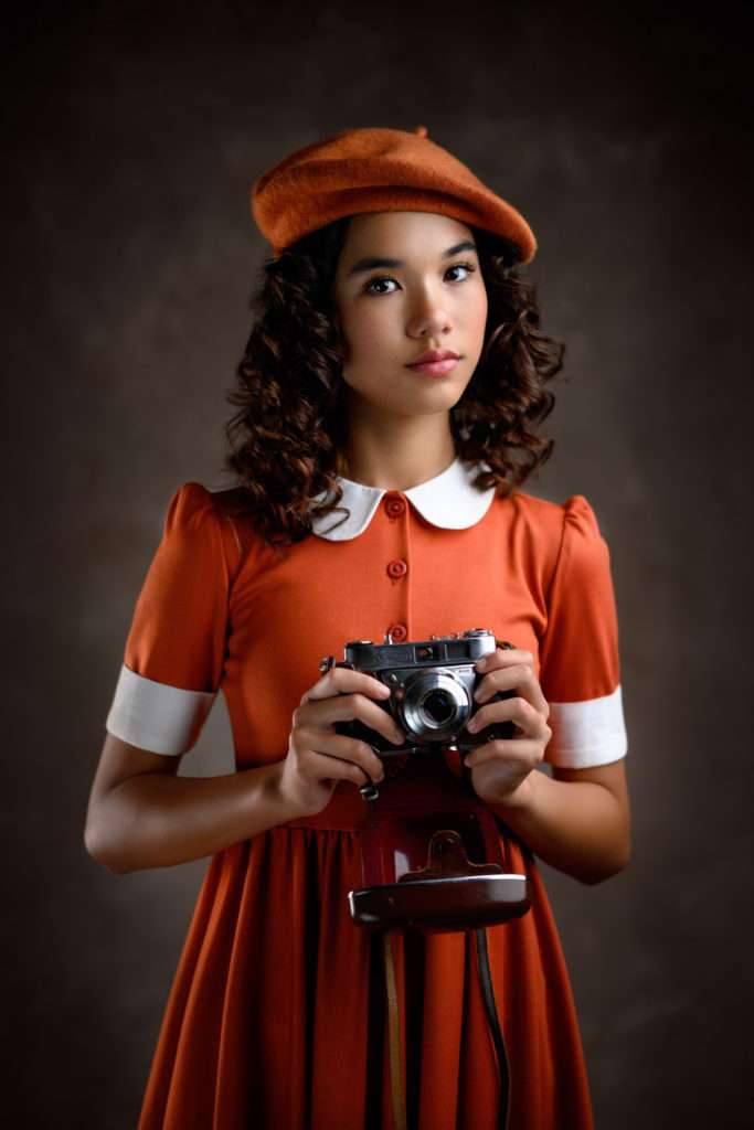 fine art portrait of a girl wearing orange dress and orange beret and holding a vintage camera