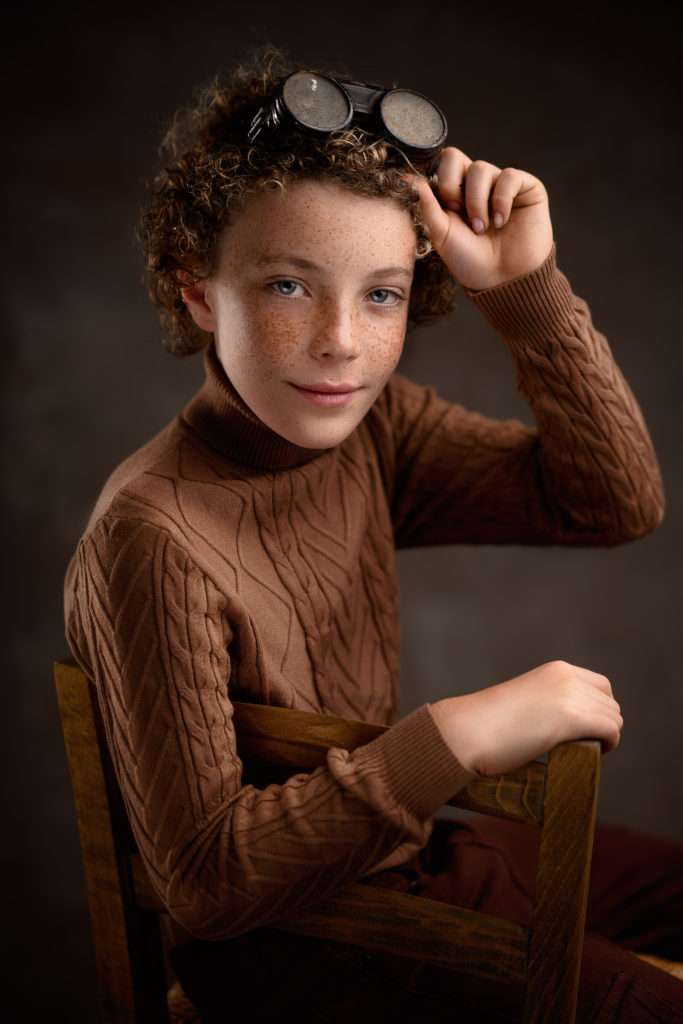 studio portrait of handsom redhead boy with curly hair and fleckles sitting on the cahir by best san diego family photographer